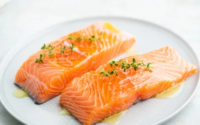 Two fresh salmon fillets on a white plate garnished with herbs.