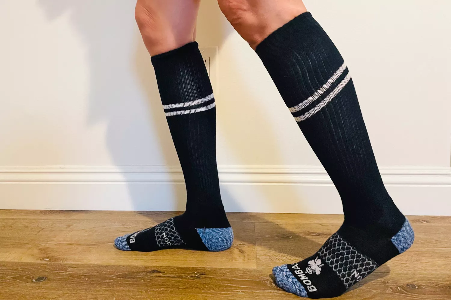 A person wearing Bombas knee-high compression socks with distinct white stripes.