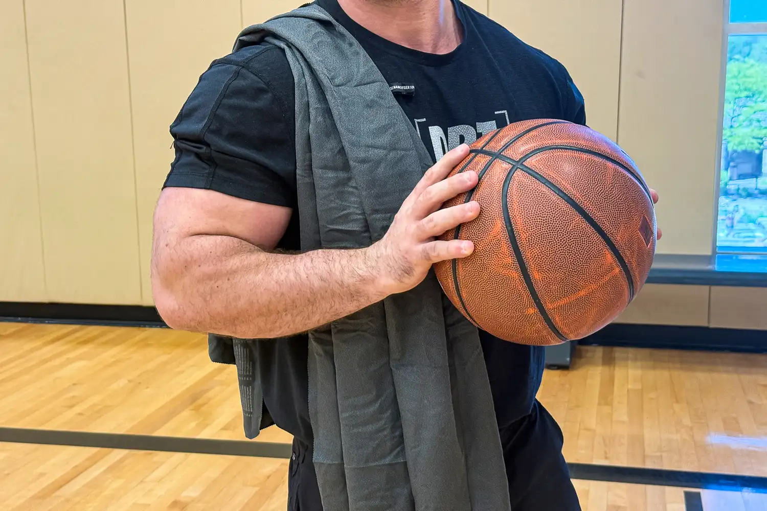 An athlete on a basketball court with a compact gray Matador Nanodry towel over his shoulder.