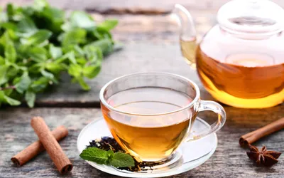 A cup of herbal tea with mint, cinnamon, and star anise on a wooden table.