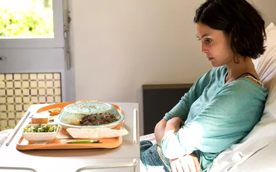 A woman in a hospital bed looking away from her meal tray during recovery.