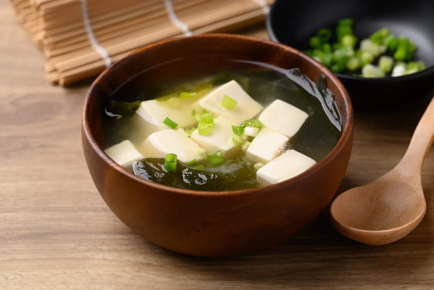 Traditional Japanese miso soup with tofu and seaweed in a dark bowl.