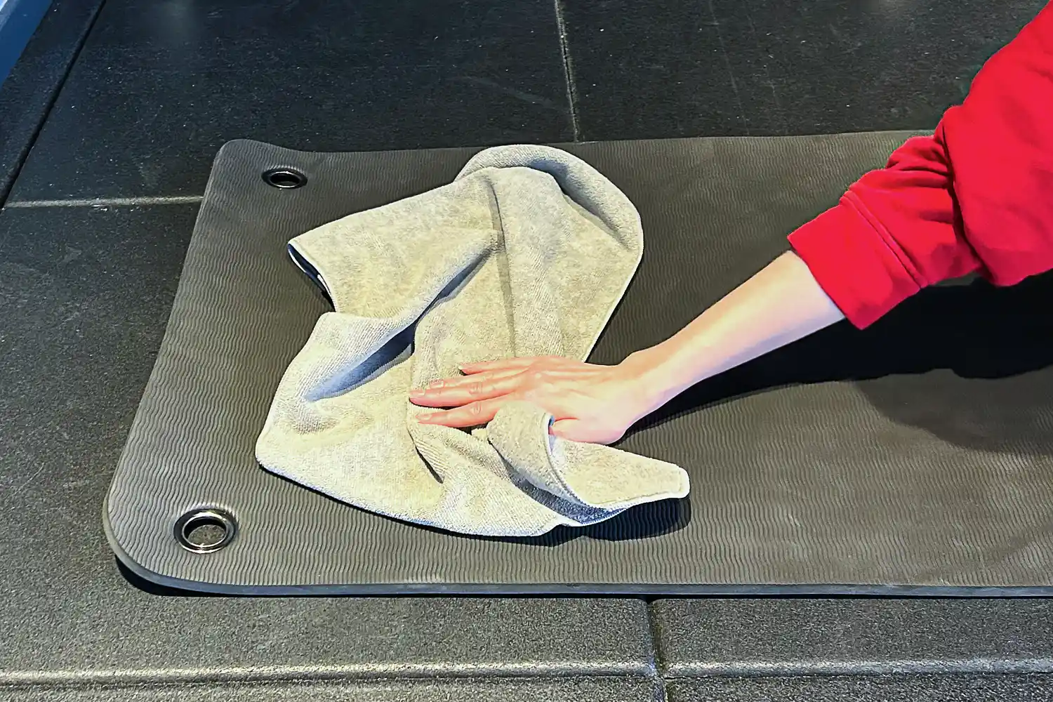 A person using a microfiber towel to wipe down a yoga mat on the floor.