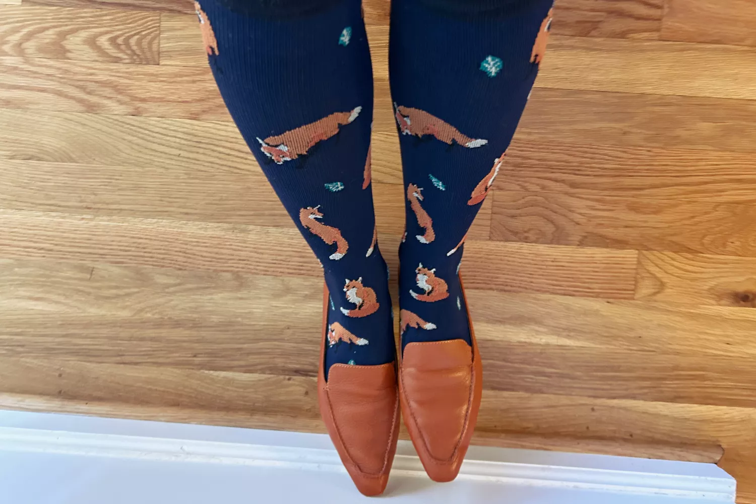 Navy blue compression socks with orange fox patterns worn with leather loafers.
