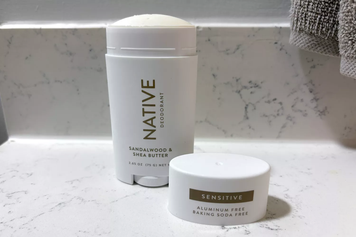 Two Native brand deodorant sticks on a marble countertop, showing the Sandalwood and Sensitive versions.