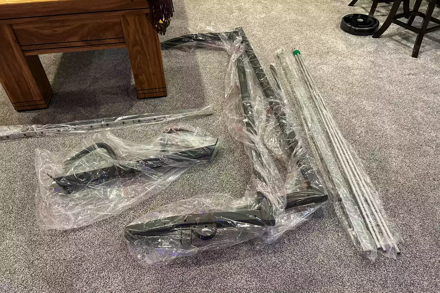 Unassembled parts of a functional trainer wrapped in plastic on a floor.