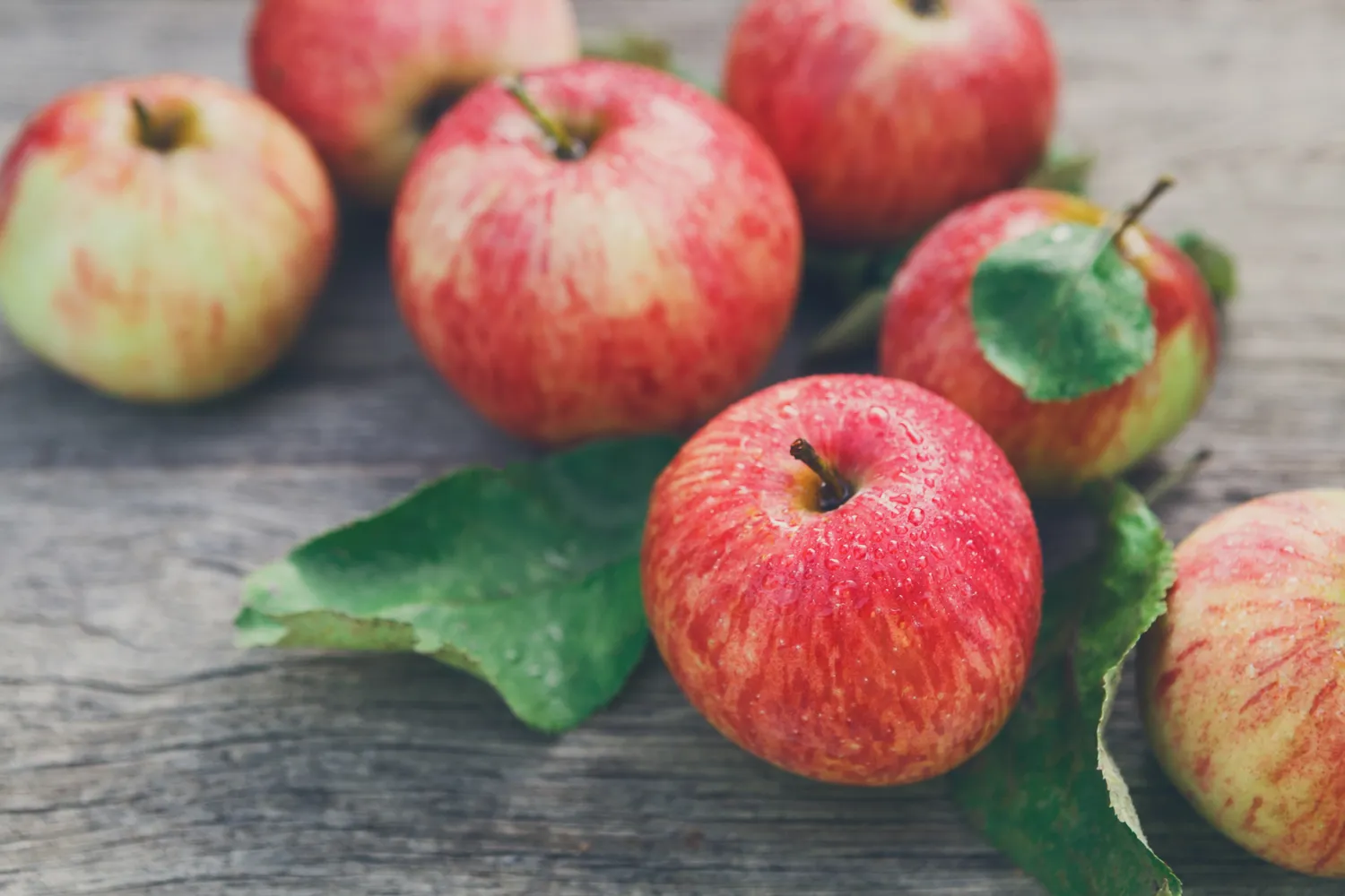 Fresh red apples glistening with water droplets on a rustic wooden surface.