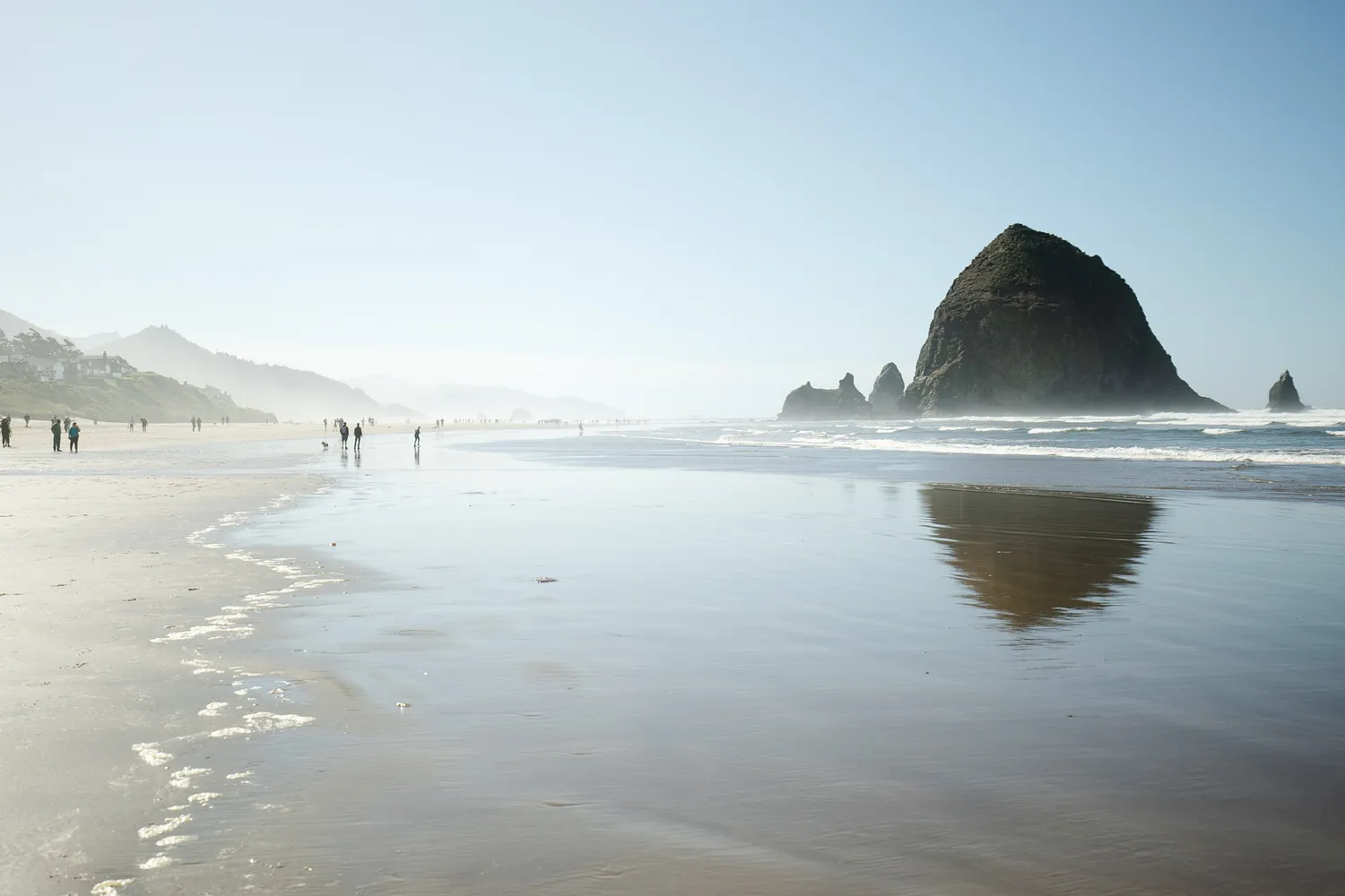 People walking on the beach at Cannon Beach Oregon with the iconic Haystack Rock in the distance.