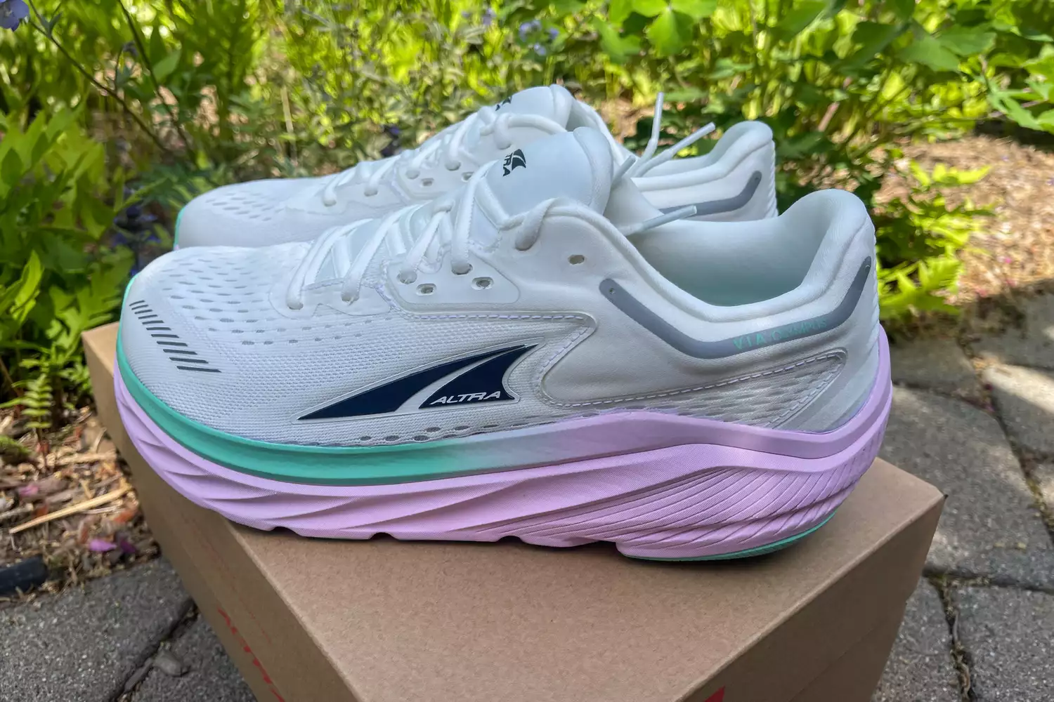 White and teal Altra VIA Olympus shoes resting on a box, highlighting the high stack height.