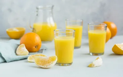 Glasses of freshly squeezed orange juice with sliced citrus fruits on a light surface.