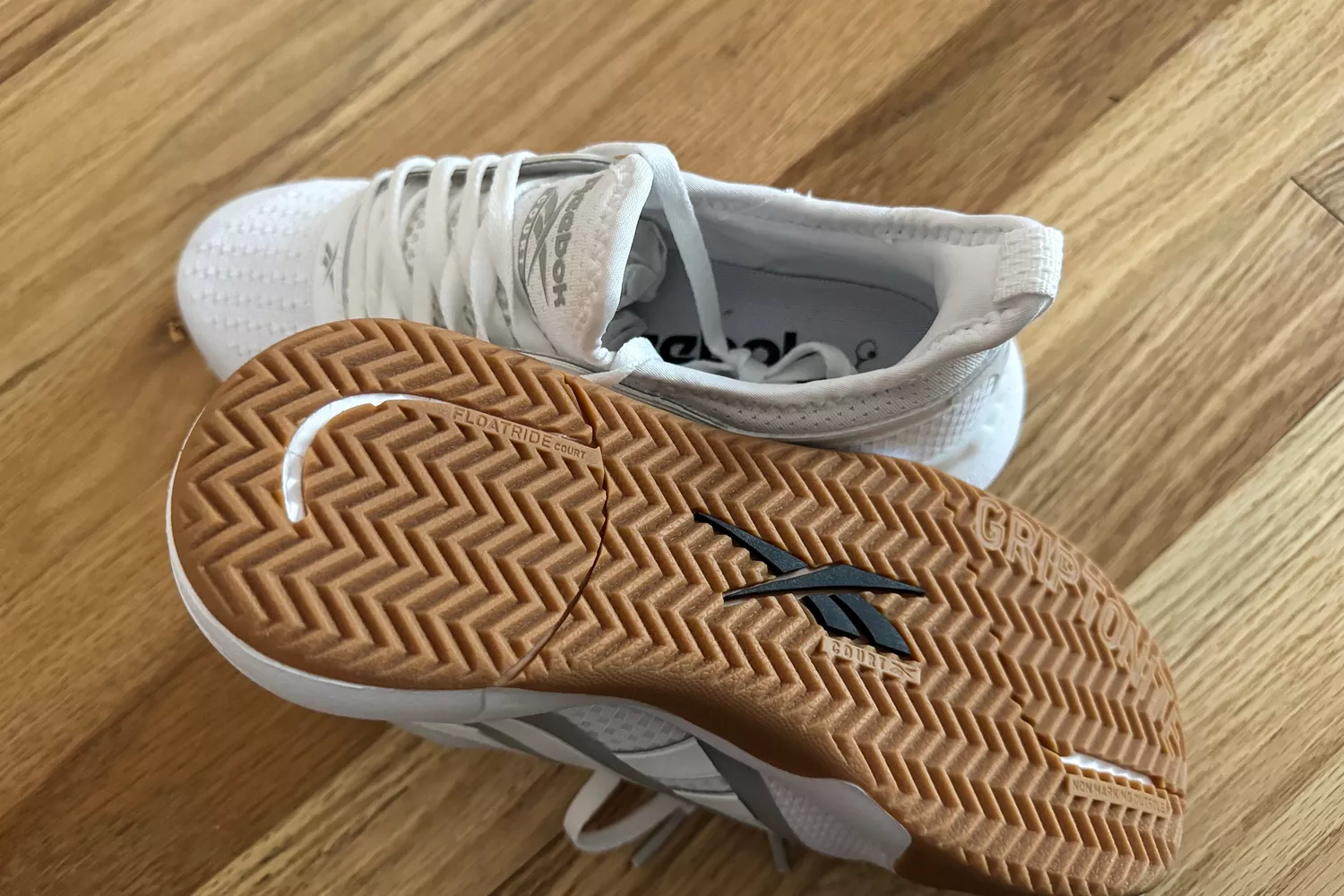 Reebok Nano Court sneakers on a wood floor, showing the tan herringbone-patterned sole.