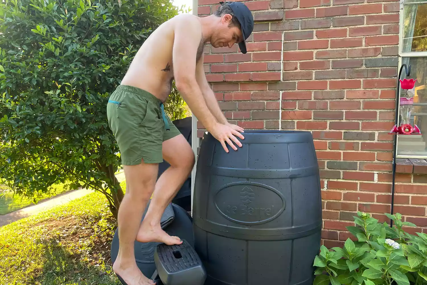 A man using a step stool to enter a tall black Ice Barrel cold therapy unit.