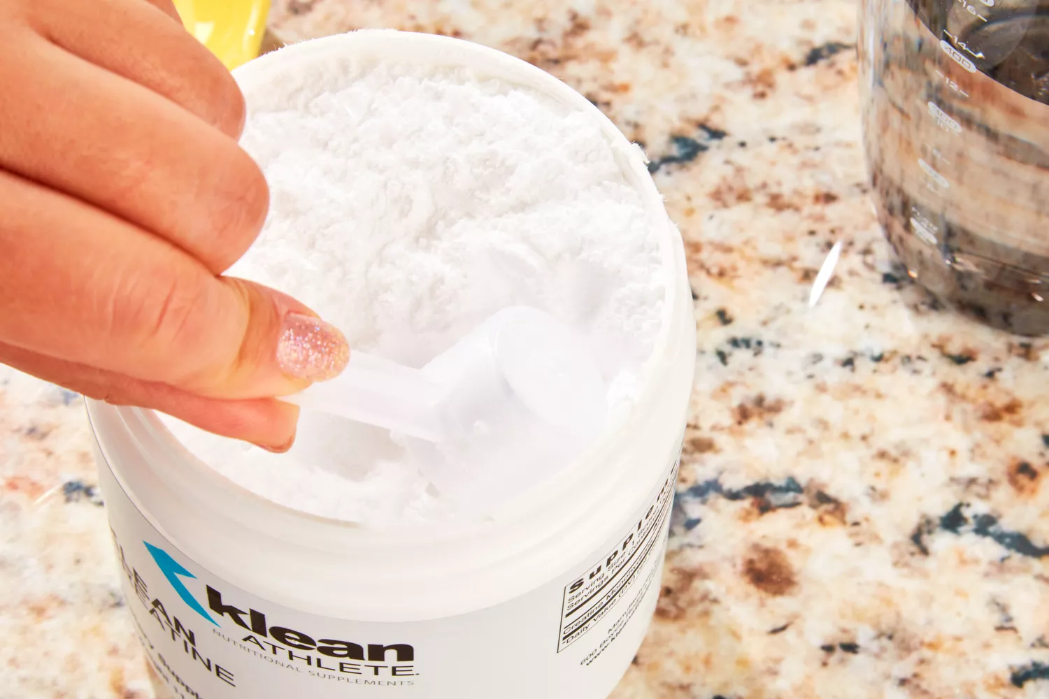 A close-up of a hand scooping white pre-workout powder from a container.