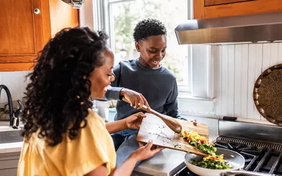 A woman and a young man preparing a fresh vegetable-based meal in a bright kitchen.