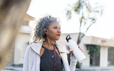 An active woman holding a white water bottle outdoors to stay hydrated.