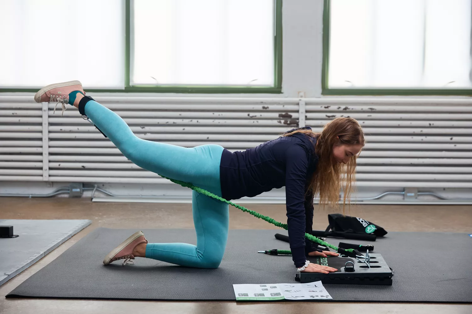 A person performing a glute bridge using the BodyBoss 2.0 portable platform and resistance bands.
