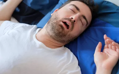 A man sleeping on a blue pillow, representing sleep-related symptoms or exhaustion.
