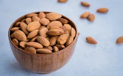 A wooden bowl filled with raw almonds on a light-colored surface.