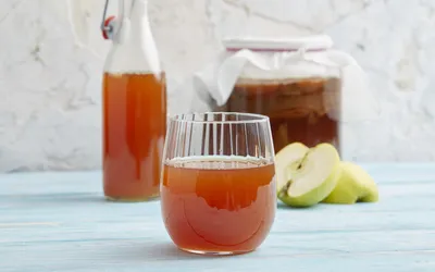A glass of amber-colored fermented kombucha next to sliced green apples.
