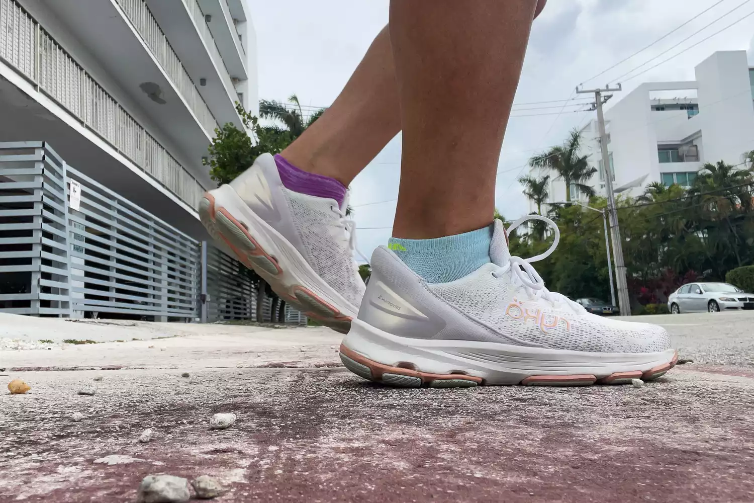 A person wearing white Ryka Devotion X walking shoes mid-stride on a city sidewalk.