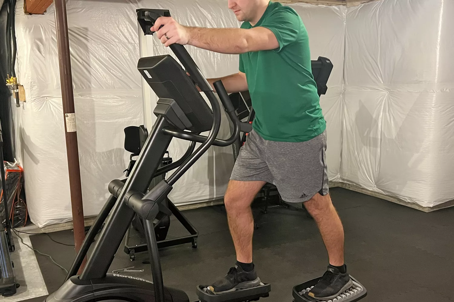 A man exercising on a NordicTrack elliptical machine in a home gym.