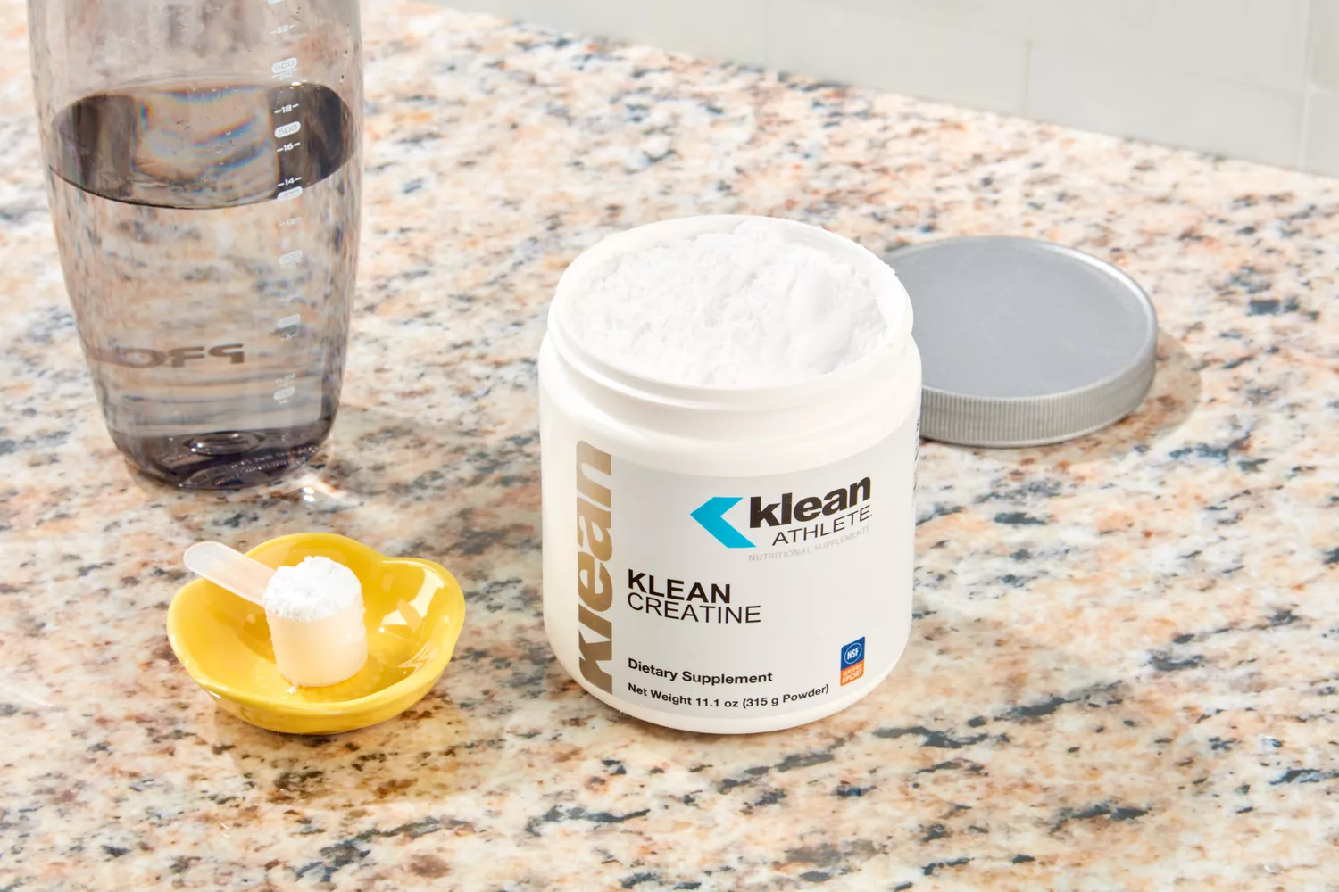 An open container of creatine powder with a scoop on a granite countertop.