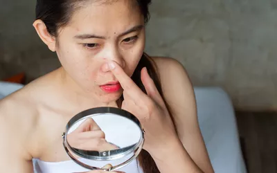 A woman closely examining her facial skin in a handheld mirror.