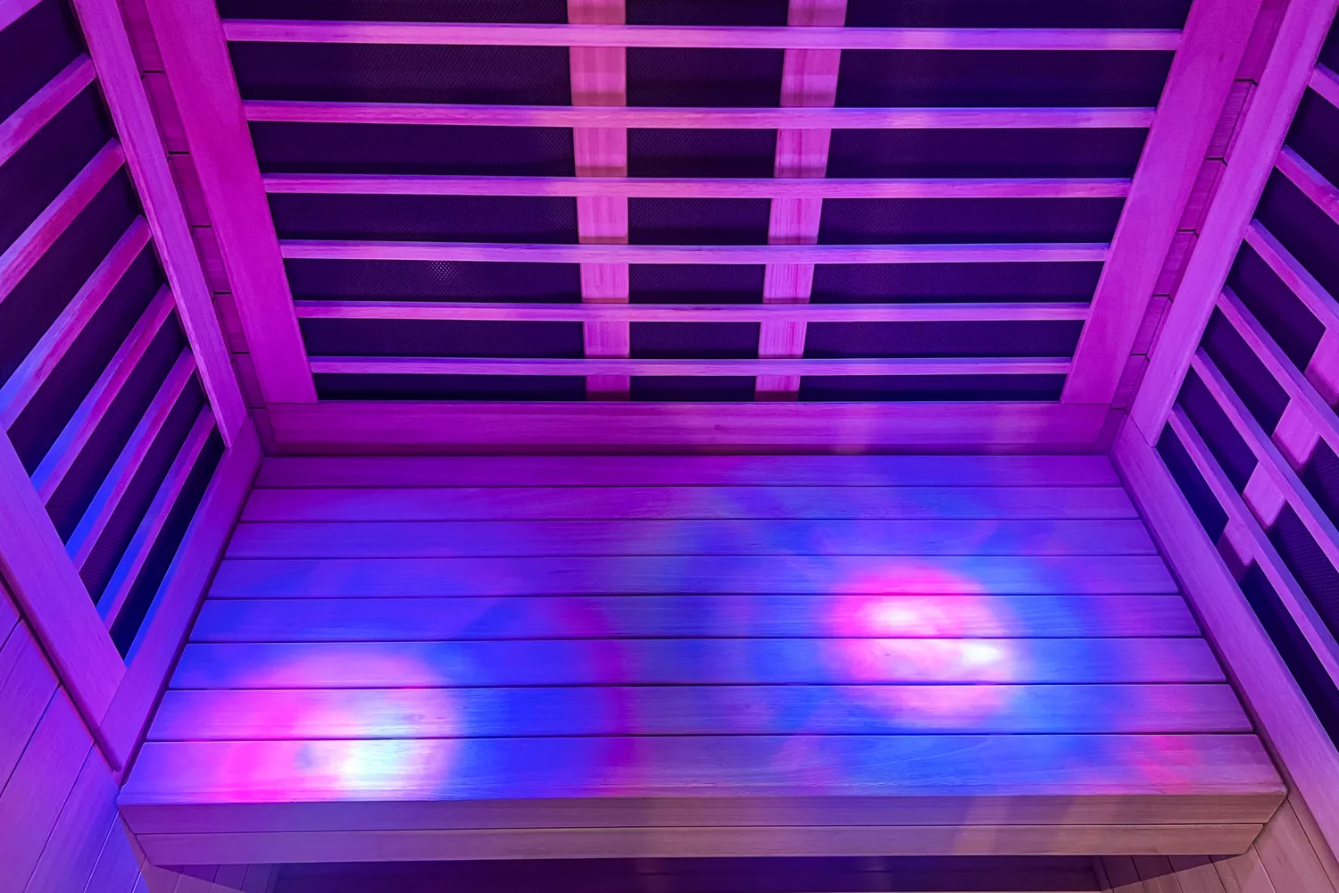 An empty wooden infrared sauna with vibrant purple and blue LED mood lighting.