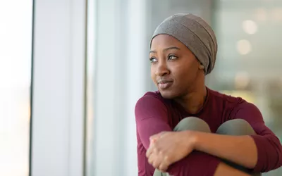 A young woman with a headscarf looking thoughtfully out a window during her recovery journey.