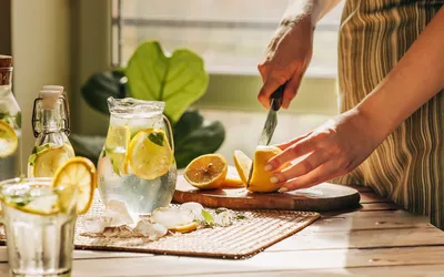 A person slicing lemons next to a pitcher of water, emphasizing a healthy hydration routine.