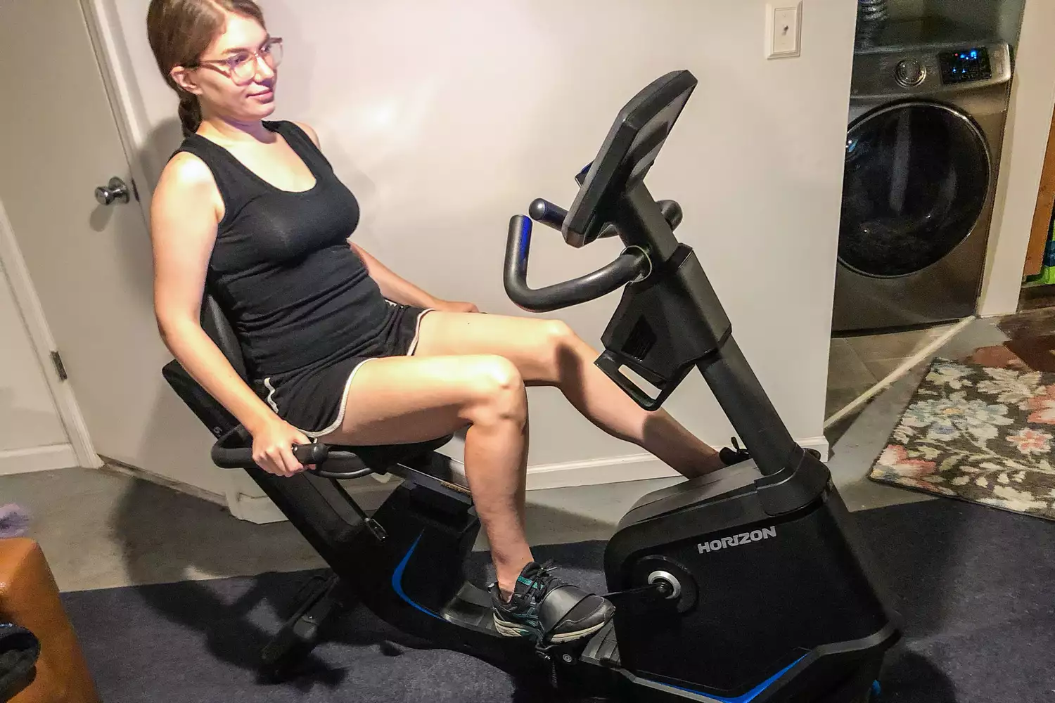 A woman using a Horizon Fitness recumbent bike in a domestic setting.