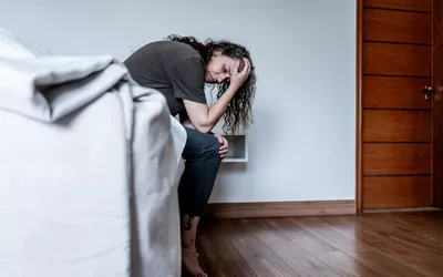 A woman sitting on her bed with her head in her hands, reflecting emotional vulnerability.