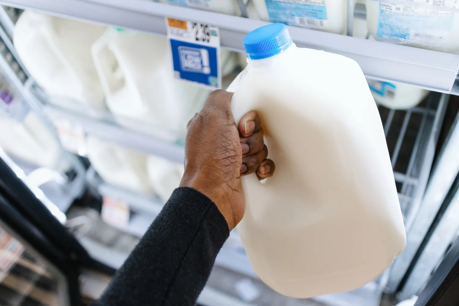 A person in a grocery store aisle holding a carton of milk.