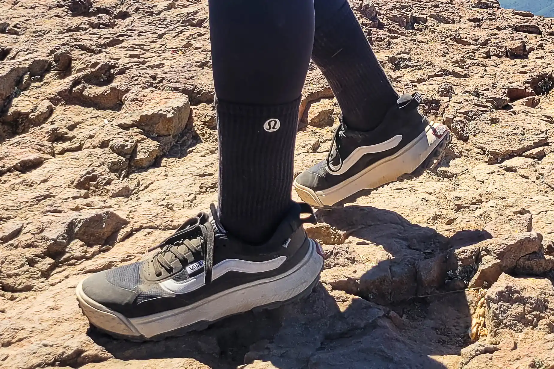A hiker wearing Lululemon socks and trail shoes navigating a rocky mountain path.