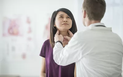 A doctor in a clinical setting examining a patient's neck area during a consultation.