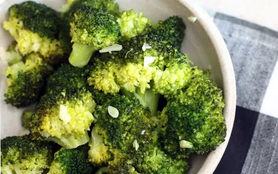 A bowl of freshly steamed broccoli with garlic on a rustic cloth.