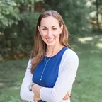 A smiling fitness professional standing in a natural outdoor setting.