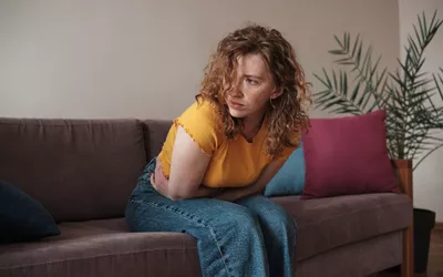A woman sitting on a couch holding her stomach in visible discomfort.