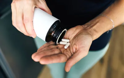 A person pouring white health supplements into their hand.