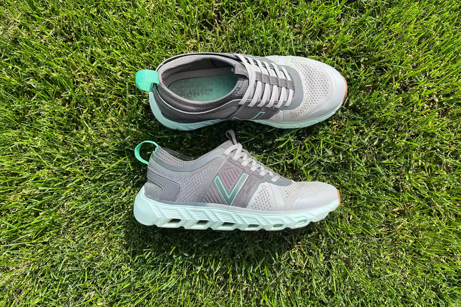 A pair of white Vionic Captivate sneakers placed on green grass.
