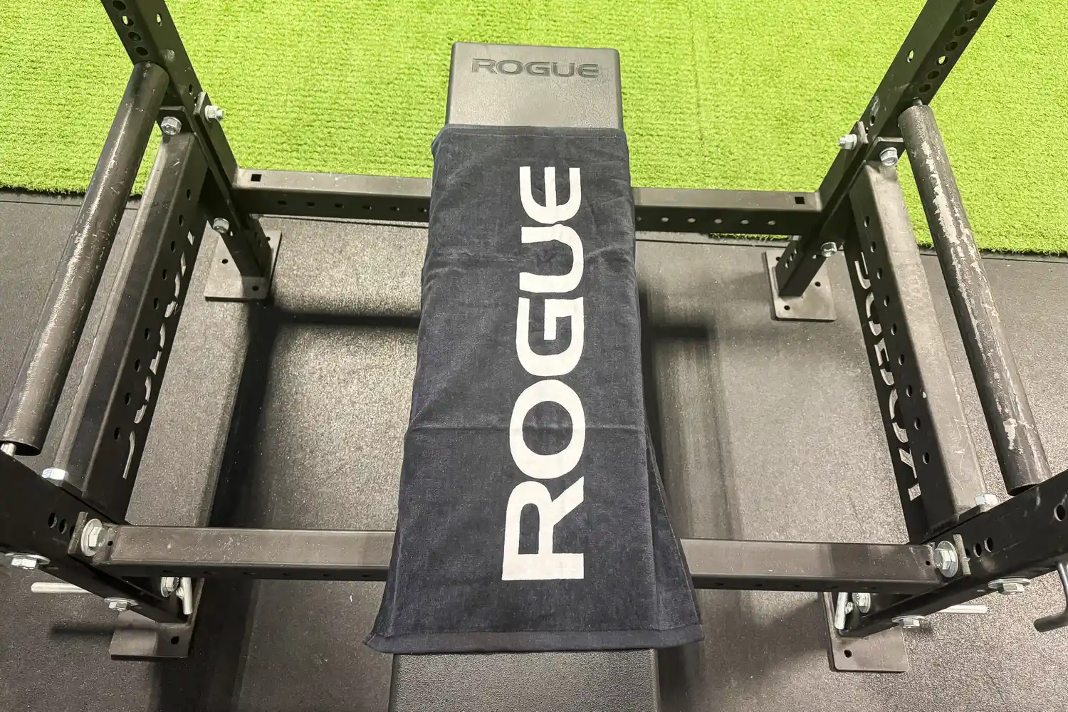 A black Rogue gym towel draped over a weight bench in a power rack.