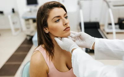 A healthcare professional wearing gloves palpating a patient's neck to check the thyroid gland.