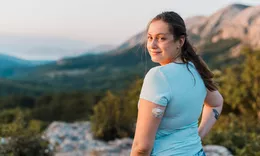 A woman wearing a CGM hiking a mountain trail at sunset.